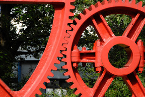 Zahnräder Campus Nord_01 Die Zähne von zwei großen roten Zahnrädern aus Stahl verhaken sich.
